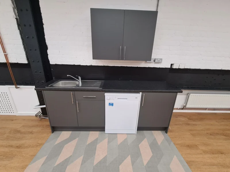 A small kitchen unit with a sink, fridge, and storage cupboards.