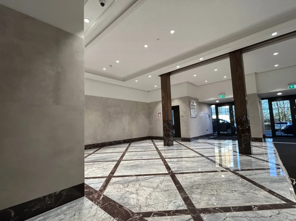 Wide view of a grand lobby featuring polished marble floors, dark wood pillars, and a recessed spotlight ceiling.