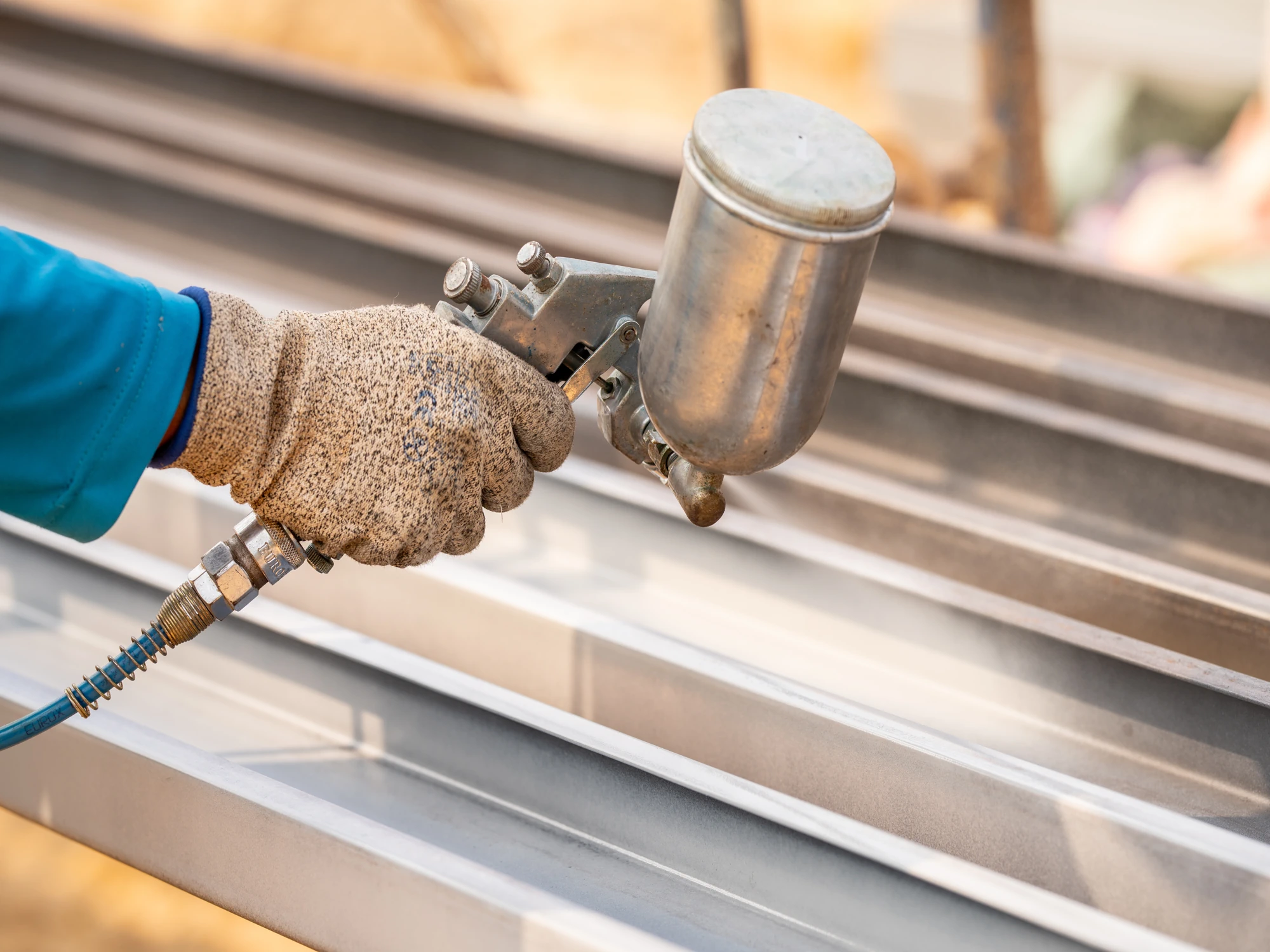 Contractor using metallic spray gun to apply anti-corrosion coating to cladding.