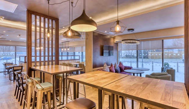 Open-plan bar and restaurant space with high wooden tables, contemporary pendant lighting, and large windows.