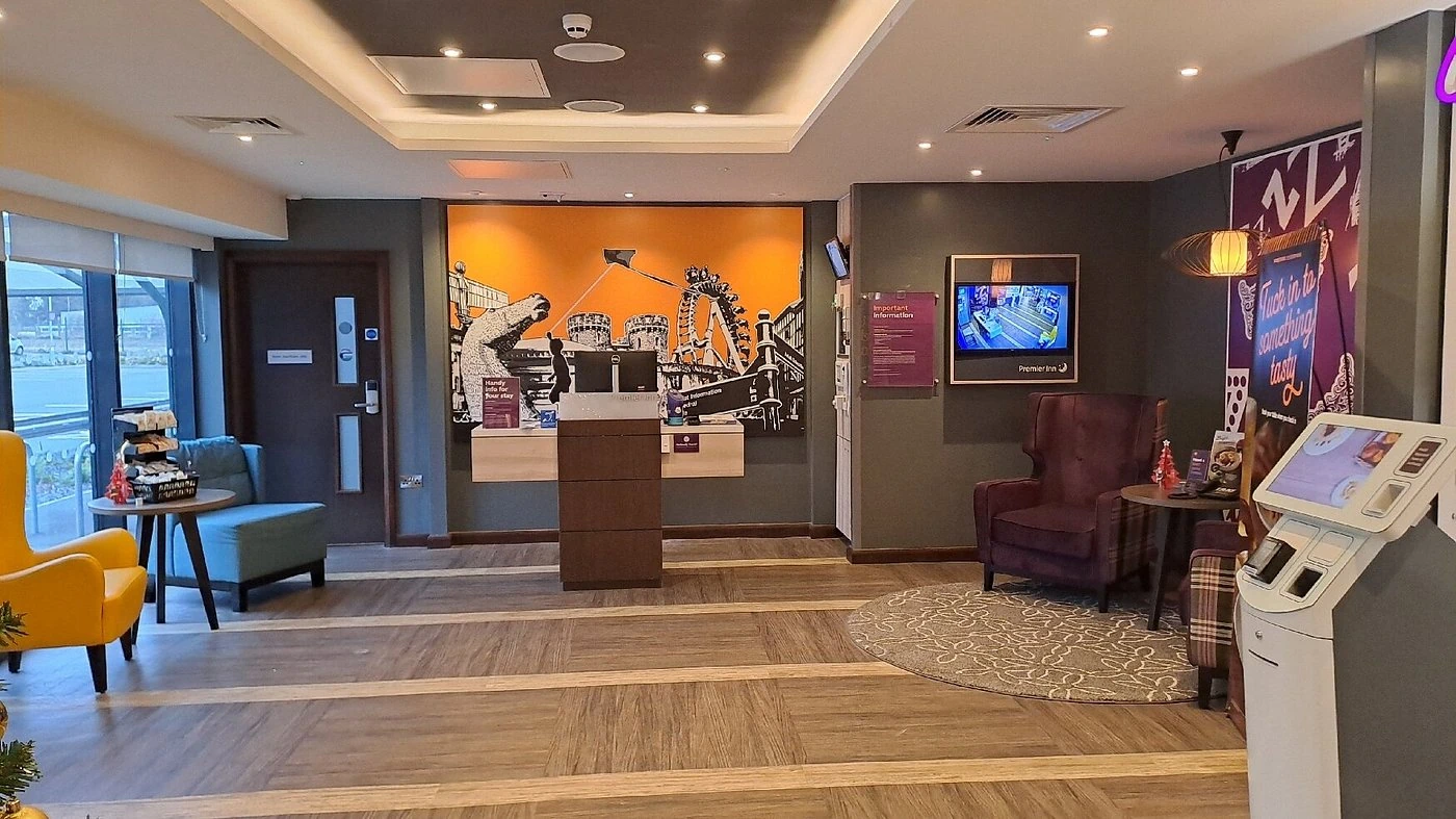 Hotel lobby area with automated self-check-in kiosks, purple armchairs, and a large Alnwick-themed mural.