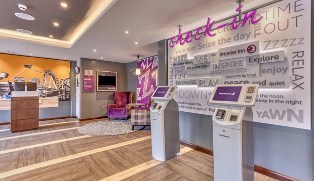 Hotel lobby area with automated self-check-in kiosks, purple armchairs, and a large Alnwick-themed mural.