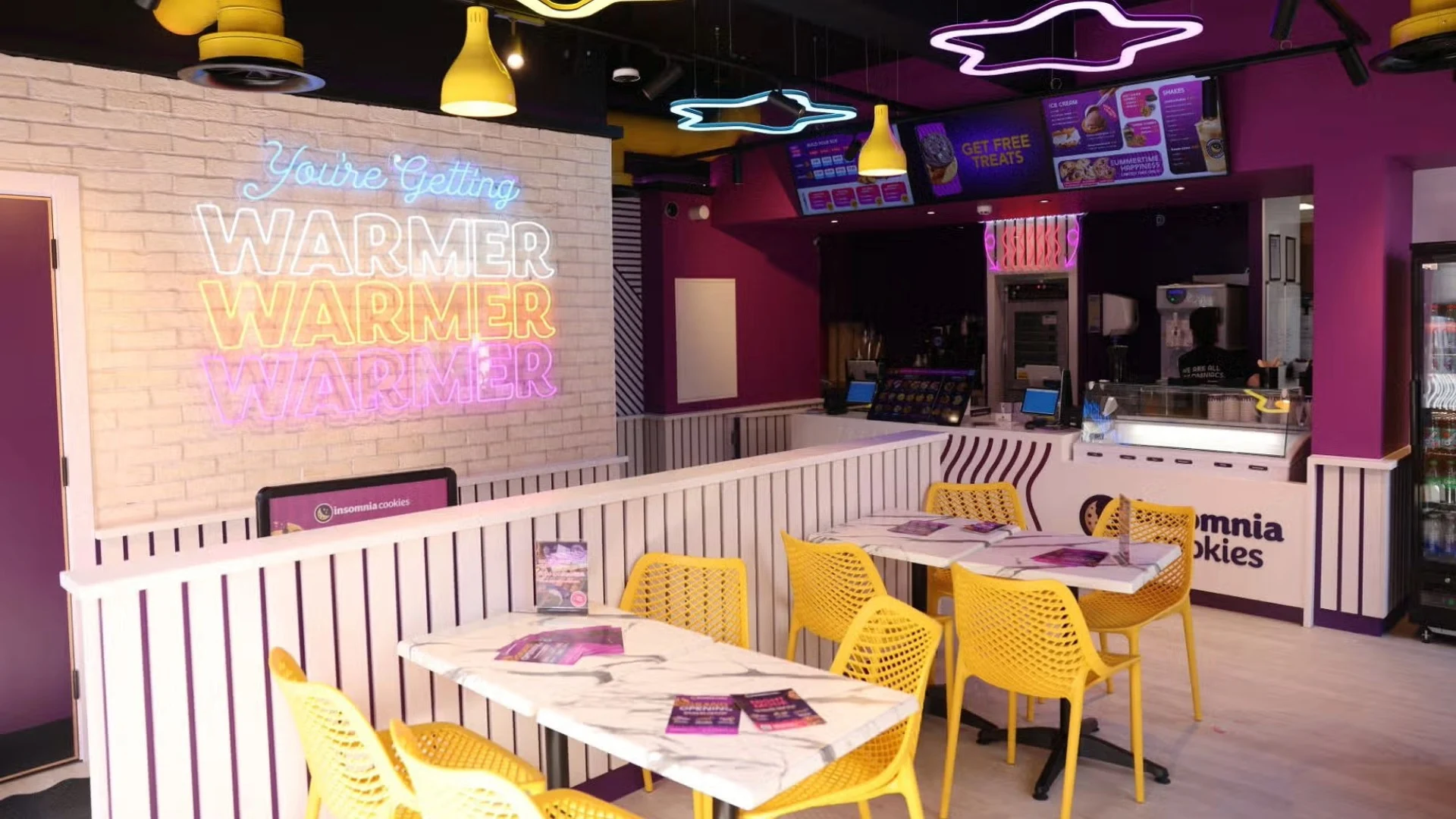 The inside of Insomnia Cookies’ Newcastle store, with bright colours and an illuminated sign.
