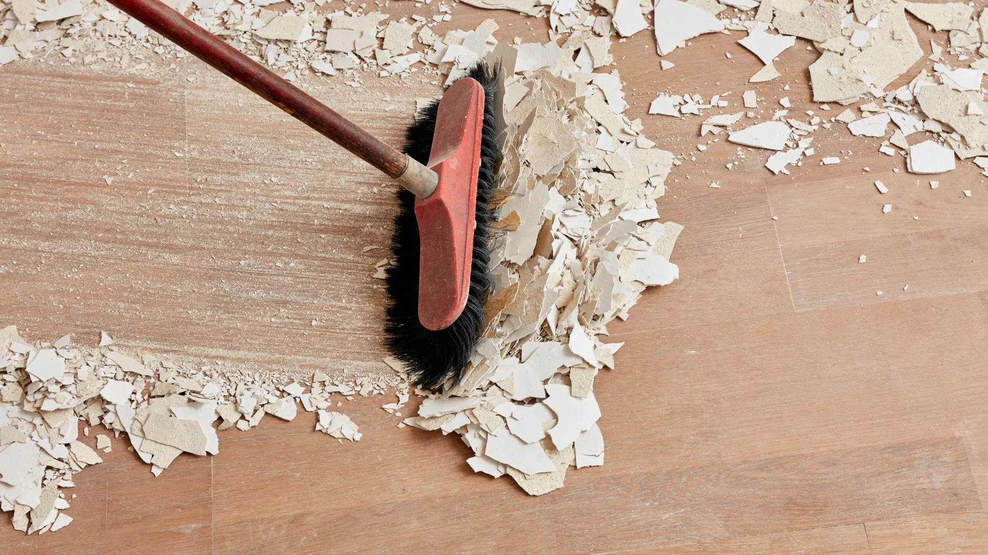A red broom sweeping debris on a wooden floor after a renovation.